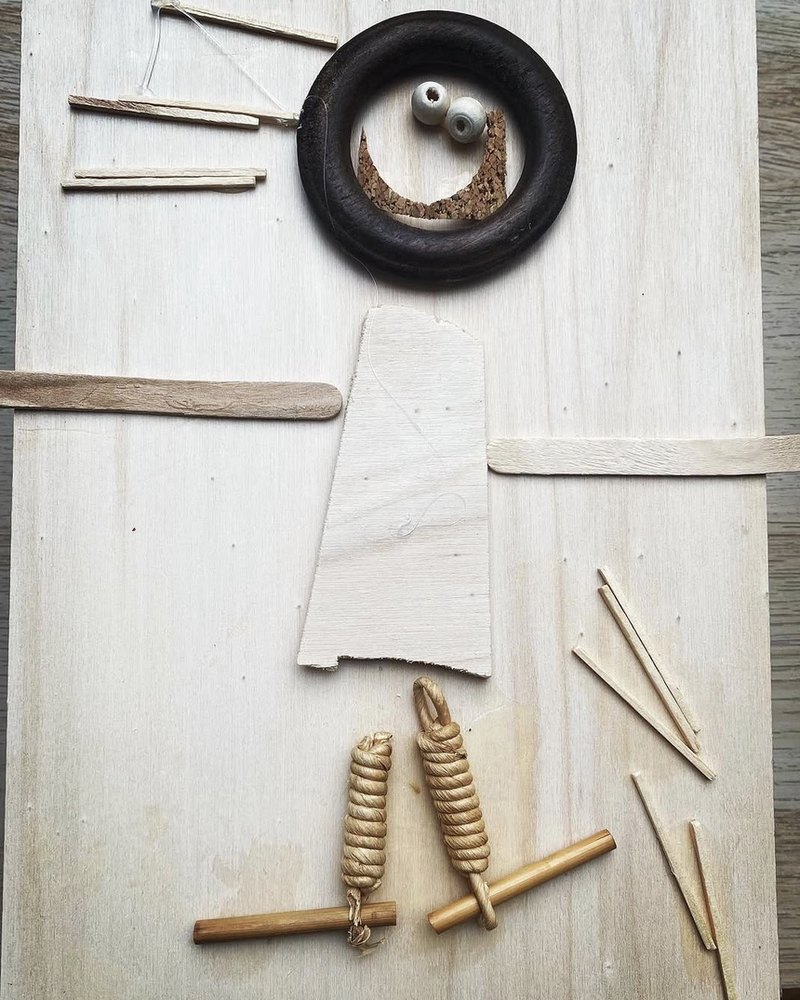 Un collage fatto da una bambina con legnetti, spago, sughero e un anello di legno, che compone una figura sorridente