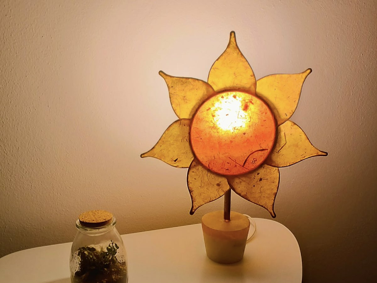 Une lampe en forme de soleil allumée sur une petite table, à côté d'un bocal en verre avec une plante
